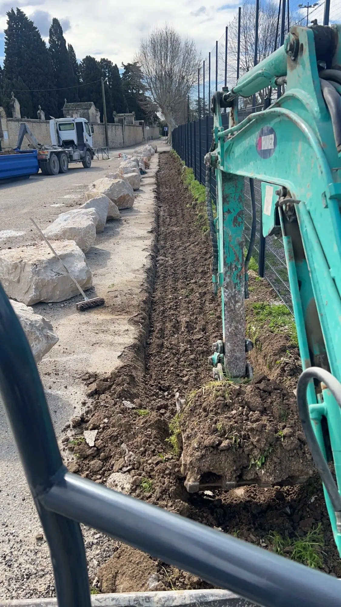 Pose des blocs de pierre à la minipelle le long de la clôture du stade