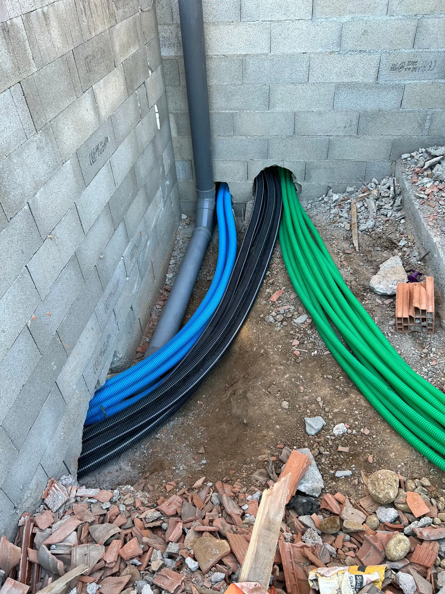 Faisceau de gaines bleues, vertes et noires sortant en attente au pied d’un mur